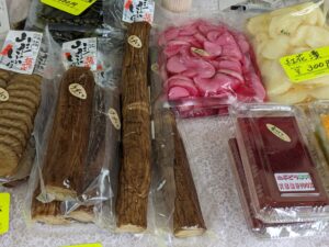 Assorted Japanese preserved vegetables in clear packaging: brown burdock roots, pink pickled radish, and white root slices on a patterned surface.